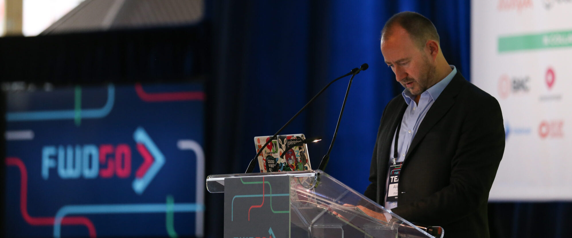 A picture of me standing at a lectern, working on a laptop computer, on the stage of the FWD50 digital government conference